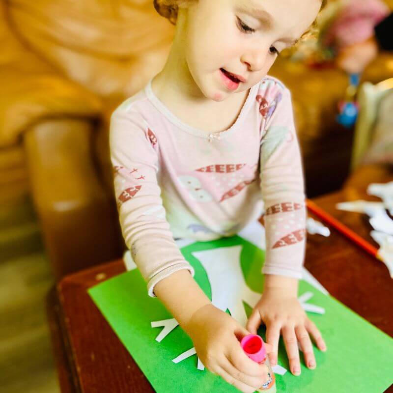 child gluing paper tree to construction paper